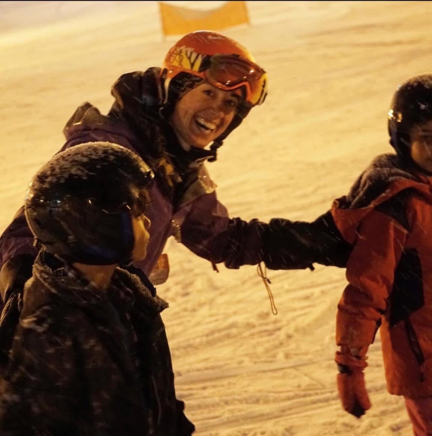 A volunteer instructor high-fiving a young skier on the snow at night.